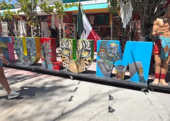 Letras gigantes de TULUM decoradas con motivos mayas junto a una estatua de un guerrero y la bandera de México
