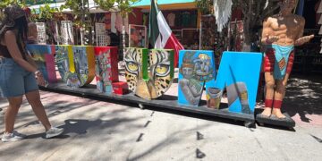 Letras gigantes de TULUM decoradas con motivos mayas junto a una estatua de un guerrero y la bandera de México